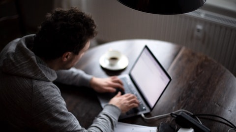 Ein Mann sitzt im Homeoffice am Tisch an einem Laptop und arbeitet. Spätestens durch die Pandemie hat sich Homeoffice bei Unternehmen und Kommunen als Arbeitsform etabliert. Aber bleibt es auch in Zukunft dabei oder kommt es zu einer Rückkehr der Mitarbeitenden ins Büro?