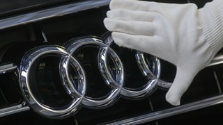 Hand streicht über Logo des Autobauers Audi.
