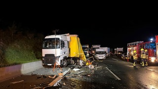 Ein Lkw, der auf dem Standstreifen steht, ist hinten völlig kaputt. Daneben stehen weitere Fahrzeuge und die Feuerwehr. Bei einem tödlichen Unfall auf der A3 bei Wertheim beging der Unfallverursacher Fahrerflucht.