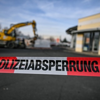Ein Bagger steht nach einer Zerstörungsfahrt neben einem Autohaus in Tauberbischofsheim hinter einer Polizeiabsperrung (Archivbild). Jetzt richten sich die Ermittlungen der Staatsanwaltschaft gegen fünf Polizeibeamte, die die tödlichen Schüsse gegen einen Baggerfahrer abgegeben haben sollen. 