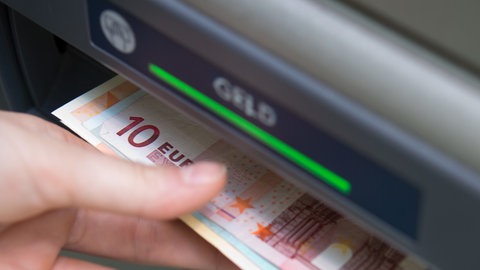 Eine Hand nimmt Geldscheine aus einem Geldautomaten. In Eppingen wurde eine Frau im Vorraum einer Bank eingesperrt. Dann ging der Alarm los.