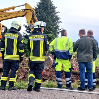 Einsatzkräfte der Feuerwehr stehen vor dem Bagger an der Stelle, wo das Gas in Mainhardt ausgetreten ist. Bauarbeiter hatten damit die B14 lahm gelegt.
