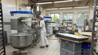 Ein Mann steht vor einer großen Knetmaschine in einer Backstube. Bäcker müssen oft auch sonntags ran, um Brötchen zu backen.
