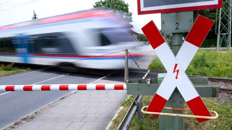 Ein Zug fährt an einer geschlossenen Bahnschranke vorbei (Symbolbild). Bei Wittighausen ist ein Regionalexpress in einen gefällten Baum gekracht. 200 Reisende saßen im Zug fest. Er wurde evakuiert.