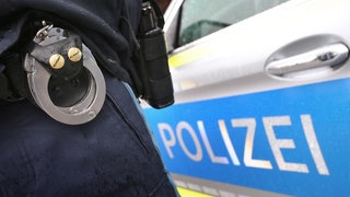 Ein Polizist mit Handschellen vor einem Polizeiauto. Eine Frau konnte vor ihrem Exfreund fliehen, nachdem dieser sie in Künzelsau entführt hatte.