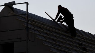 Symbolbild: Ein Dachdecker arbeitet auf einem Einfamilienhaus