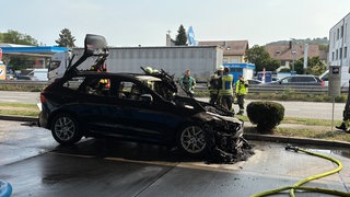 Ausgebranntes Auto an einer Neckarsulmer Tankstelle: Die Feuerwehr war mit einem Großaufgebot vor Ort, um ein Übergreifen der Flammen zu verhindern. Mehrere Gefahren drohen.
