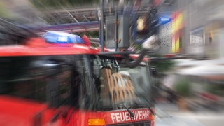 Ein Einsatzfahrzeug der Feuerwehr mit Drehleiter und Blaulicht mit Effekt-Überlagerung (Symbolbild)