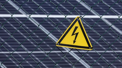 Ein Starkstrom-Warnschild vor einer Photovoltaik-Anlage (Symbolbild). Aus einem Solarpark bei Ahorn haben Diebe etwa fünf Kilometer Kabel entwendet. Der Wert liegt laut Polizei bei rund 100.000 Euro. 