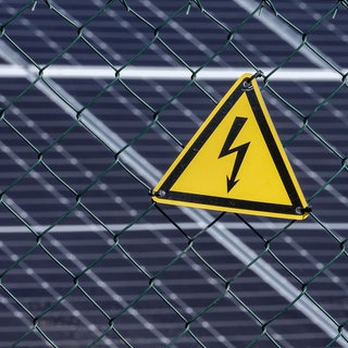 Ein Starkstrom-Warnschild vor einer Photovoltaik-Anlage (Symbolbild). Aus einem Solarpark bei Ahorn haben Diebe etwa fünf Kilometer Kabel entwendet. Der Wert liegt laut Polizei bei rund 100.000 Euro. 