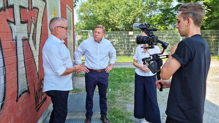 Der ehemalige Polizeioberkommissar Peter Fink (links) zusammen mit dem Landtagsabgeordneten Nico Weinmann (FDP) und Regierungspräsidentin Susanne Bay (rechts) vor der Kamera. 
