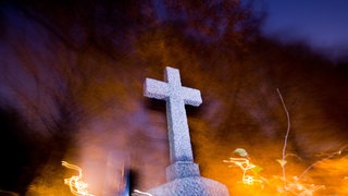 Ein Kreuz steht am auf einem Friedhofsgrab.