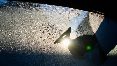 Gefrorene Autoscheibe wird von Eis befreit (Symbolbild). Ein frostiger Morgen mit Nebel: Die Winterdienste sind aber gerüstet und die und Salzlager voll. 