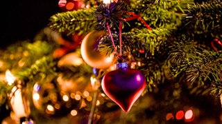 Ein Herzanhänger hängt an einem geschmückten Weihnachtsbaum. 