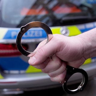 Ein Polizist hält Handschellen vor einem Einsatzfahrzeug hoch.