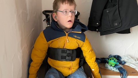 Benedikt ist mit einem Gurt festgeschnallt, damit er nicht aus dem Rollstuhl fällt.