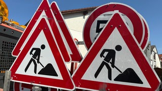 Mehrere Verkehrsschilder, die vor einer Baustelle warnen, stehen auf der Pritsche eines Transporters.