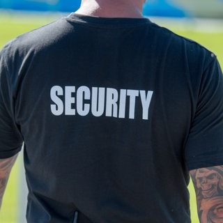 (Symbolbild) Ein Mann in einem T-Shirt mit der Aufschrift "Security" steht mit dem Rücken zur Kamera