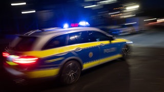 Ein Streifenwagen der Polizei fährt mit Blaulicht durch die Nacht und ist unscharf zu erkennen. (Symbolbild) Eine vermeintliche Explosion hat in Schwäbisch Hall für Verunsicherung gesorgt. Laut Polizei wurden Böller gezündet.