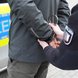 Ein Polizist legt einem Mann Handschellen an (Symbolbild). Ein 74-jähriger Pole soll in Deutschland über Jahre hinweg als Serieneinbrecher aktiv gewesen sein. 