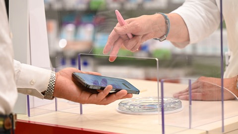 Ein Mann zeigt einer Apothekerin auf einem Handy sein E-Rezept (Symbolbild). 