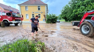 Wegen des Starkregens wurden Schlamm und Geröll durch die Straßen Binaus (Neckar-Odenwald-Kreis) gespült. Ein Mann hilft bei den Säuberungsarbeiten.