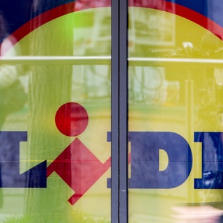 Eine Person läuft, unscharf dargestellt, an einem Schaufenster mit riesigem Lidl-Logo dahinter vorbei. (Symbolbild) Nachdem Lidl vor dem Landgericht Heilbronn erneut eine Niederlage einstecken musste, will das Unternehmen mit Sitz in Bad Wimpfen (Kreis Heilbronn) in Berufung gehen. Es geht um Irreführung bei Preisen im Prospekt.