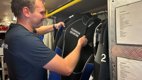 Feuerwehrazubi Philipp Bauer nimmt einen Taucheranzug aus dem Schrank in einem Feuerwehrfahrzeug.