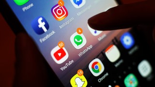 Ein Jugendlicher hält ein Smartphone in der Hand, auf dem verschiedene Social Media Apps angezeigt werden (Symbolbild).