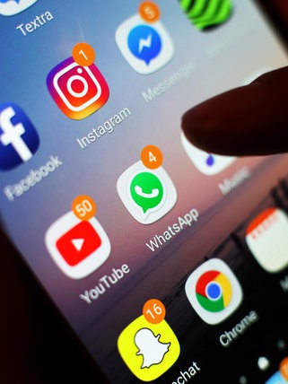 Ein Jugendlicher hält ein Smartphone in der Hand, auf dem verschiedene Social Media Apps angezeigt werden (Symbolbild).