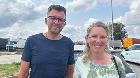 Ein Paar steht bei ihrem Auto der Raststätte bei Pforzheim. Sie brauchen eine Pause vom Stau.