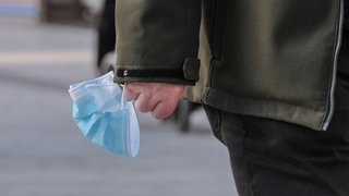 Symbolbild: Mann trägt blaue Corona-Maske in der Hand