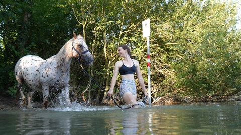 Frau badet in Karlsruhe mit Pferden in einem See