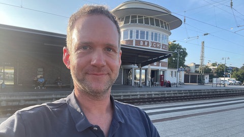 Der Reporter sitzt am Bahnhof Bruchsal und schaut in die Kamera.