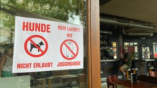 Verbotsschilder weisen schon am Eingang darauf hin: Jogginghosen sind in einem Café in Pforzheim unerwünscht