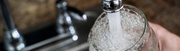 Symbolbild Wasserverseuchung mit PFAS: Wasser fließt aus einem Wasserhahn in ein Glas
