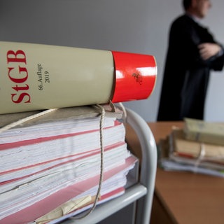 Ein Strafgesetzbuch und ein Mann in Richterrobe. Unterlassene Hilfeleistung ist ein Straftatbestand.