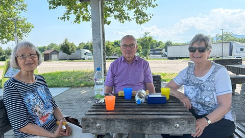 Drei Menschen sitzen an einem Tisch und essen nahe der Autobahnkirche Baden-Baden. Die Kirche steht auf einem Rasthof für Reisende der A5.