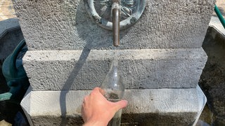Eine Glasflasche auffüllen am Trinkwasserbrunnen