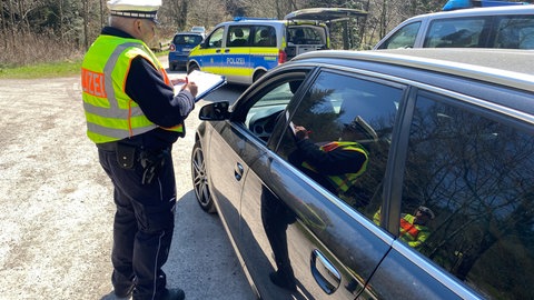 Beim Blitzermarathon 2025 in Pforzheim steht ein Polizist mit einem Klemmbrett an einem Auto, das das Fahrerfenster hinuntergelassen hat.