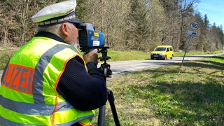 Blitzermarathon 2025 in Pforzheim: Ein Polizist steht mit einer Radarpistole an einer Straße und misst die Geschwindigkeit von einem Auto.
