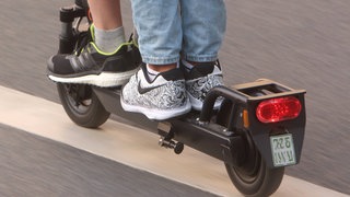 Symbolfoto E-Scooter-Unfall: Zwei Personen fahren auf einem E-Scooter