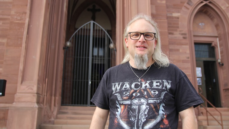 Ideengeber des Headbanger Gottesdienstes in Bruchsal-Obergrombach: Pastoralreferent Mathias Fuchs steht vor der Kirche in Obergrombach in einem Wacken Shirt.