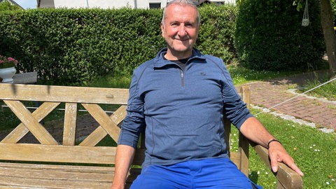 Gartenbesitzer Artur Busch sitzt entspannt auf einer freischwebenden Bank in seinem Garten.
