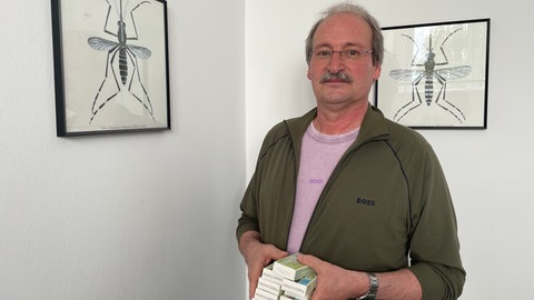 Der wissenschaftliche Direktor der KABS, Dirk Reichle, hält einen Stapel BTI-Tabletten in der Hand. Er steht neben einer Grafik der Asiatischen Tigermücke.