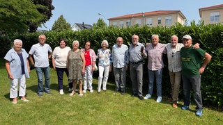 Elf der zwölf Geschwister stehen im Garten. Ein Bruder hält ein Handy mit der einzigen Schwester in der Hand, die per Video aus Kanada zugeschaltet ist.