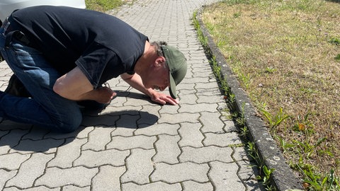 Ein Mann kniet auf einem Gehweg. 