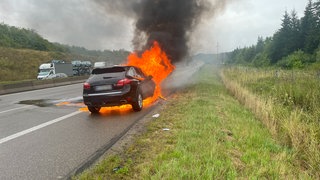 Ein Auto steht auf der Autobahn und brennt