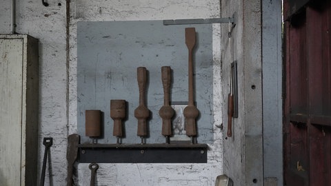 An der Wand in der Glocken-Klöppel-Schmiede hängen 5 Stahl-Elemente, die die Entstehung eines Klöppels symbolisieren.