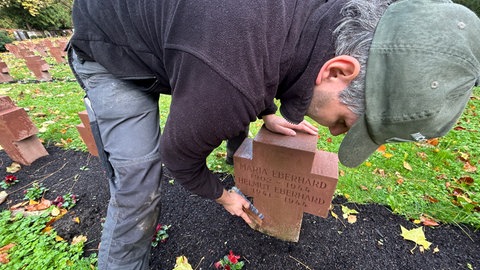 Ein Mann putzt vor Allerheiligen auf dem Hauptfriedhof in Karlsruhe einen Grabstein.